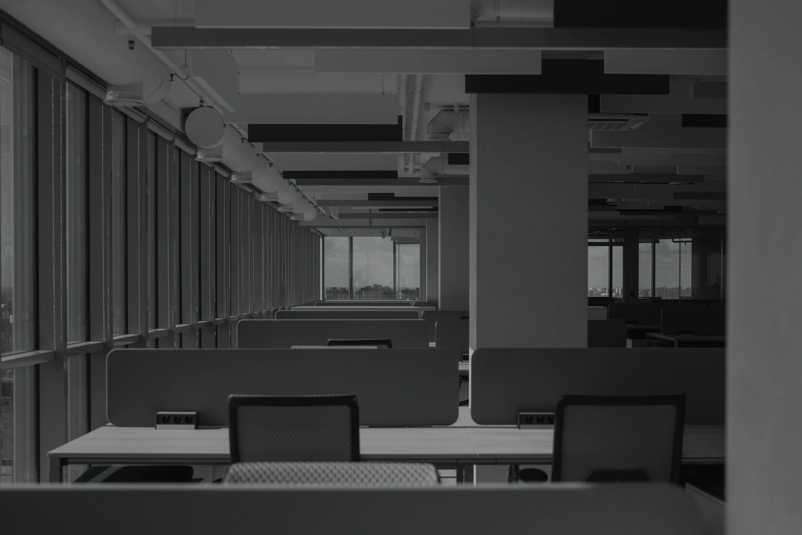 Rows of empty desks running the length of an open office floor, the structure that carries the work when nobody is standing over it